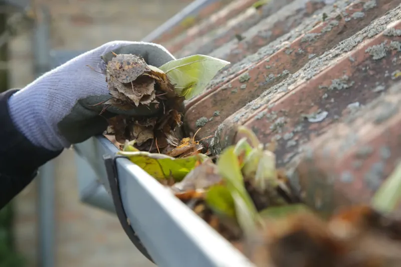 Gloved hand clearing leaves from a blocked gutter